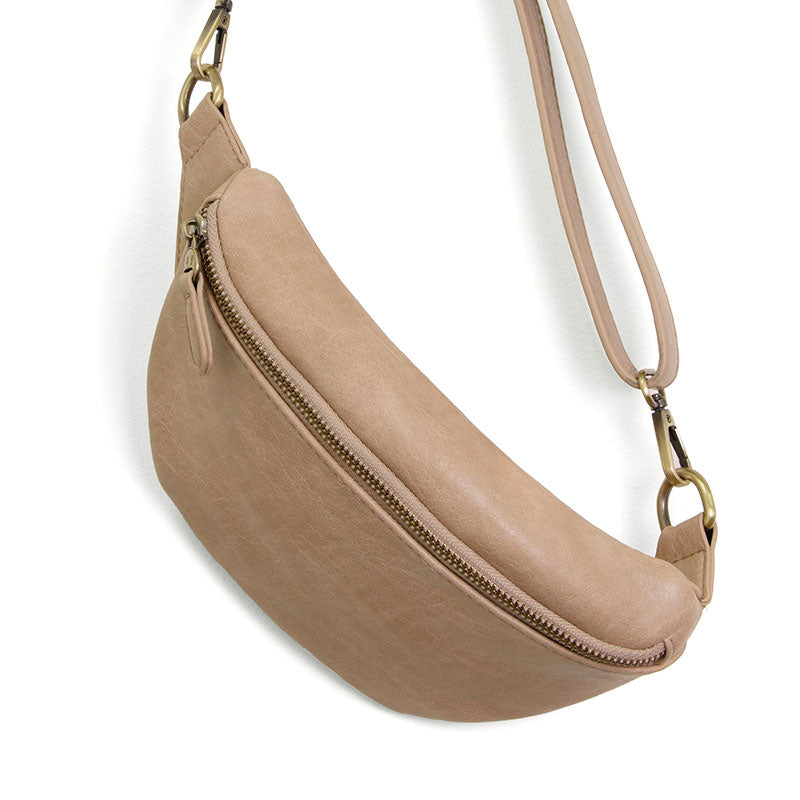A beige belt bag with a sling/belt strap, featuring a top zip closure and brass plated hardware, made from vegan leather.