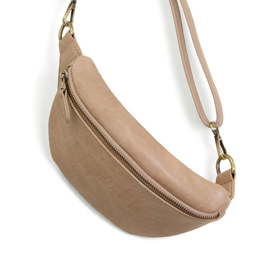 A beige belt bag with a sling/belt strap, featuring a top zip closure and brass plated hardware, made from vegan leather.